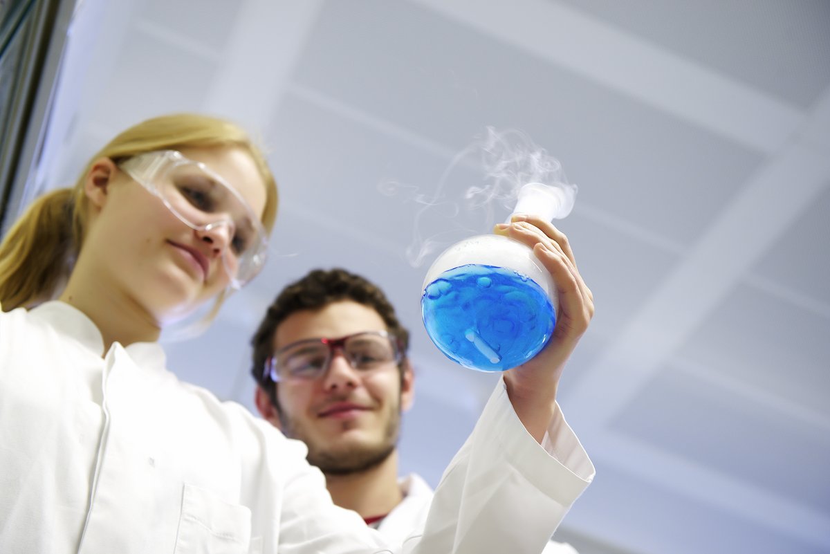 Zwei Studierende halten einen Glaskolben mit blauer Lösung
